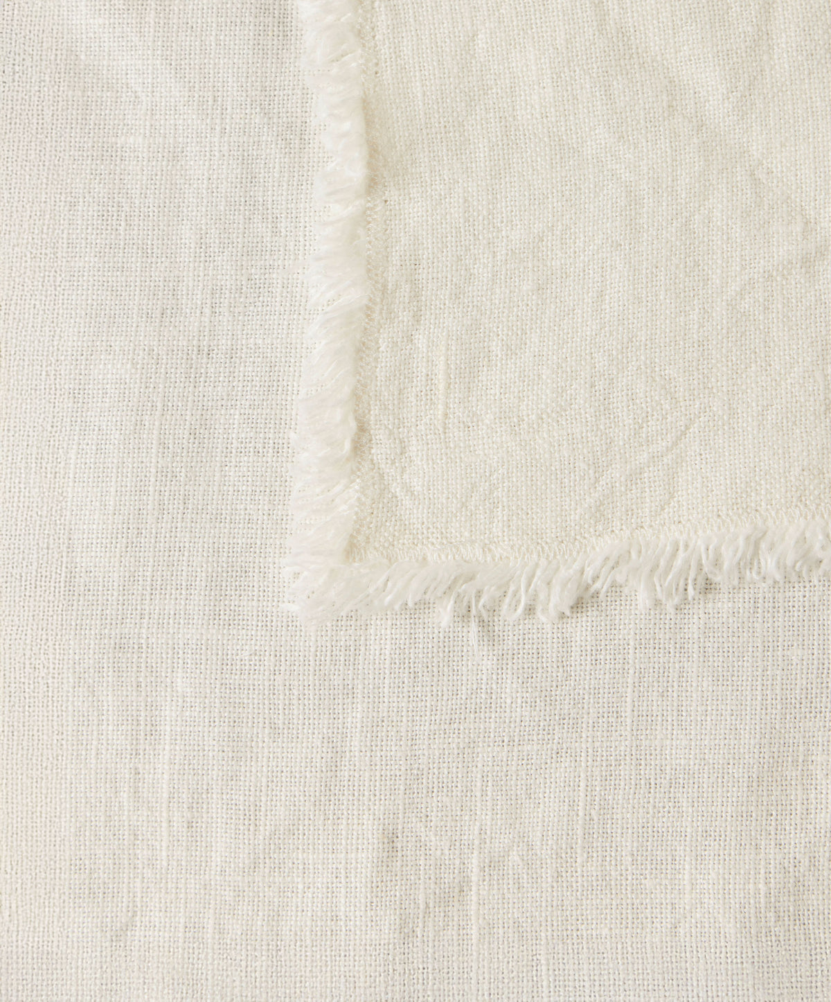 A close-up of a light beige woven fabric with a slightly frayed edge, placed diagonally over a similar textured background.