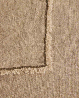 A close-up of two overlapping Fia Kitchen Towels in Pine, one arranged diagonally atop the other. Both towels are crafted from OEKO-TEX certified linen, showcasing a textured surface and finished with frayed, decorative edges.