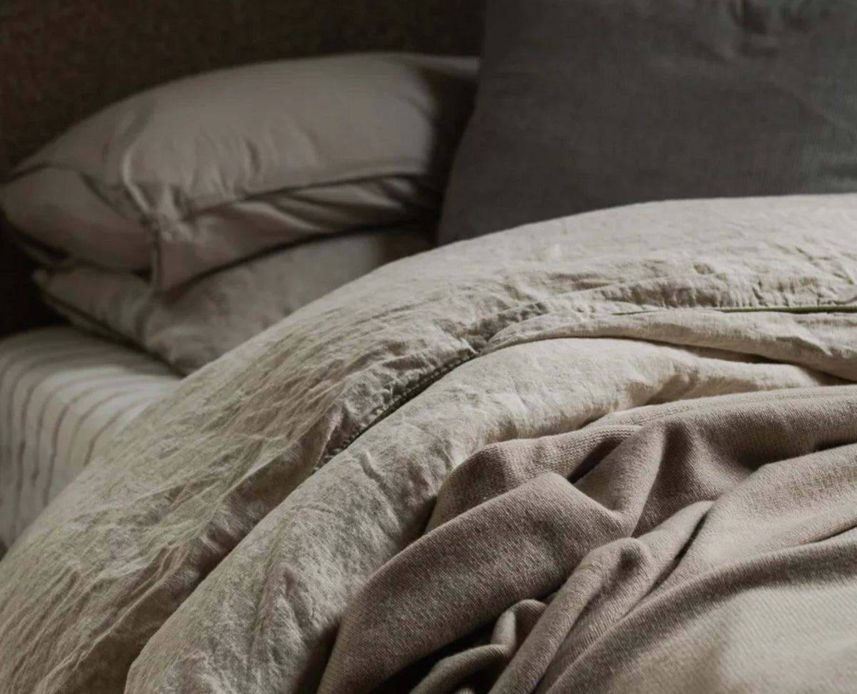 A close-up of an unmade bed with beige and gray sheets, blankets, and pillows, creating a cozy and inviting atmosphere.