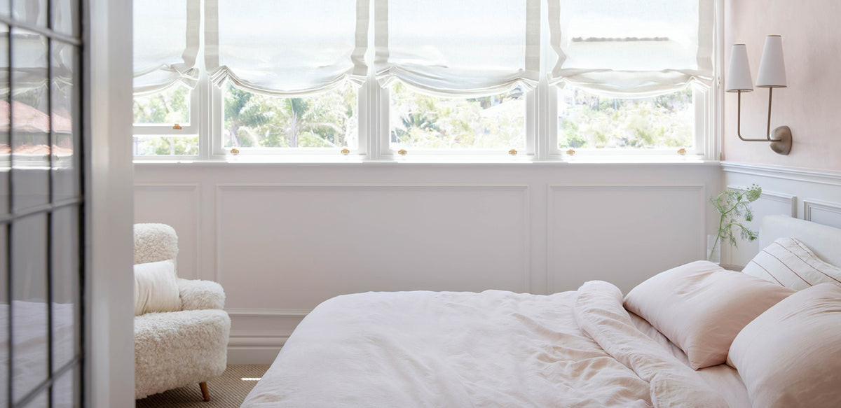 Neatly made bed in a bright bedroom with large windows.