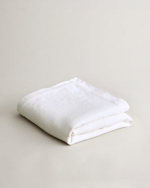 The Heavyweight Linen Bedcover - White, crafted from premium European linen and OEKO-TEX certified for safety, is neatly folded and displayed on a plain, light-colored surface under soft lighting with minimal shadows.
