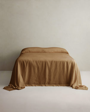 Heavyweight linen bedcover in sand color draped over a bed, showcasing its soft texture and stylish design by CULTIVER.
