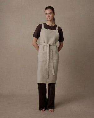 Natural Jude Linen Apron by CULTIVER displayed on a hanger, showcasing its light, breathable linen fabric and simple, functional design.