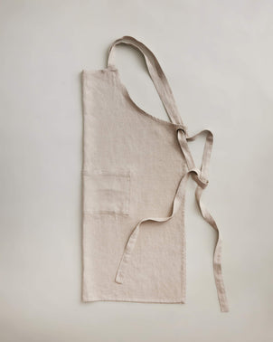 Natural Jude linen apron by CULTIVER displayed flat, showcasing its lightweight, breathable fabric and simple, elegant design.