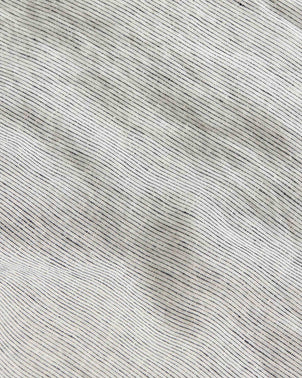 Close-up of the Linen Flat Sheet - Pinstripe made from European flax linen, featuring thin, irregular black horizontal lines that form a subtle wavy pattern. The OEKO-TEX certified fabric appears slightly wrinkled and textured.