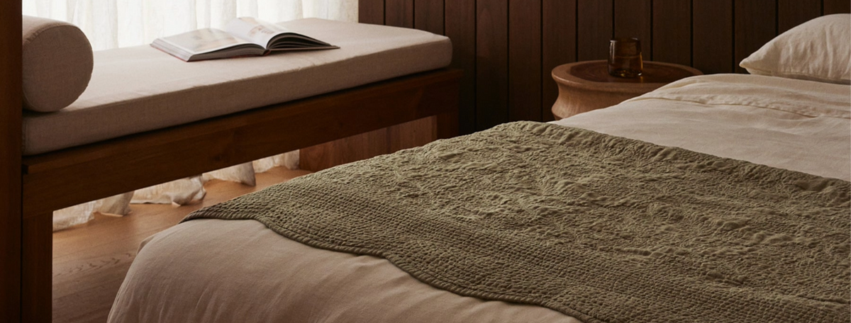 Bedroom with a bed covered in a green blanket, wooden bench, and open book.