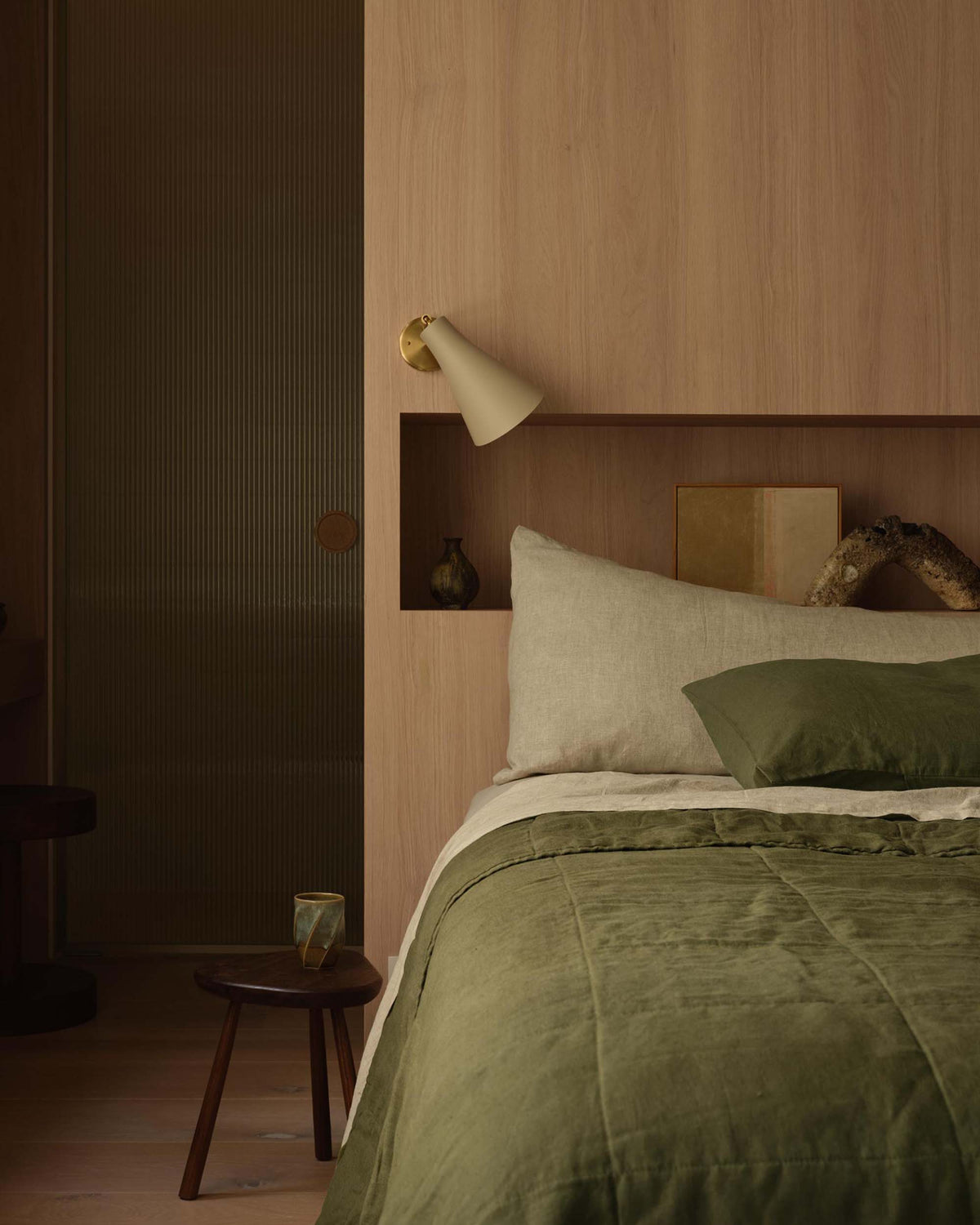 Bedroom with green bedding and wooden headboard, dimly lit.