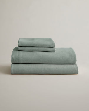 Folded sage-colored linen sheet set with pillowcases from CULTIVER, showcasing smooth, natural-texture bed linen.