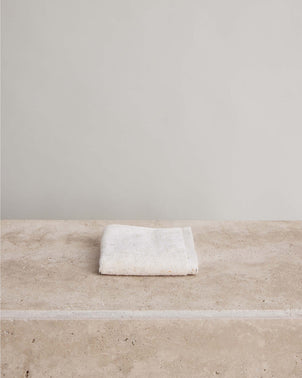 A neatly folded Woven Speckle Cotton Wash Cloth made from OEKO-TEX certified cotton rests on a beige stone surface, with a plain light gray wall in the background.