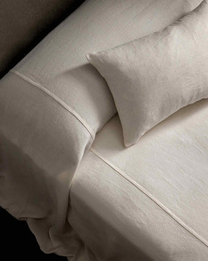 A close-up view of a neatly made bed with the Heavyweight Linen Bedcover in Ivory and a matching pillow, featuring an oversized design that highlights the smooth texture and minimal aesthetic, evoking European luxury bedding.